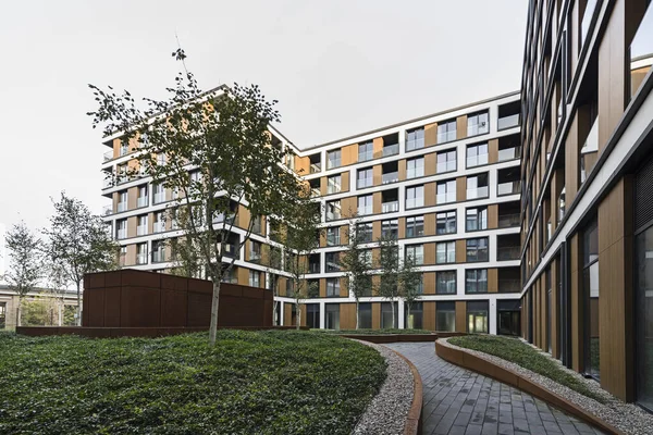 Bir Avrupa şehrinde konut binaları. Modern apartman blokları. Bahçede bitki örtüsü ve ışıklandırma var. Paslı metal kaplama, korten. Yeraltı garajı