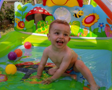 Oğlum plastik havuzda suyla oynuyor.