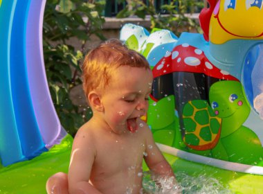 Bebek bahçedeki plastik havuza su sıçratıyor.