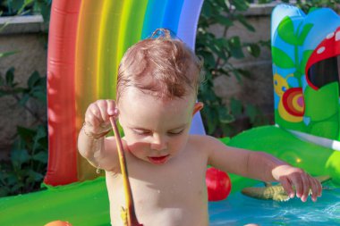 Güneşli bir günde havuzda pasif hayvanlarla oynayan bir çocuk.