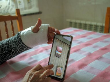 Alçılı kollu yaşlı kadın bilgi almak için cep telefonunu izliyor.