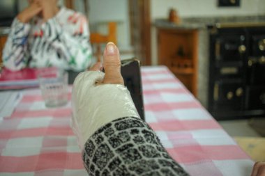 Alçılı kollu yaşlı bir kadın bilgi almak için evde cep telefonunu izliyor.