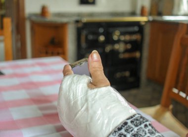 Alçılı kollu yaşlı bir adam cep telefonunu izliyor.