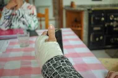 Alçılı bileği ve cep telefonu olan yaşlı bir adam mutfağında.