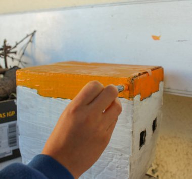 Bir çocuk karton bir kutu boyuyor ve bir ev yapıyor.