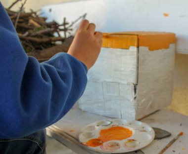 Ergen, kartondan yapılmış bir evi boyarken iyi vakit geçiriyor.