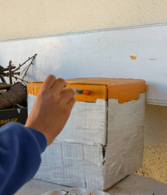 Bir okul projesi için karton ev boyayan bir genç.