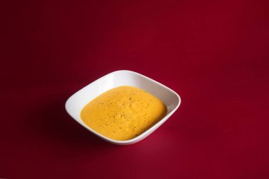 Kırmızı boyalı ahşap bir masa üzerinde kırmızı boyalı bir tabakta ezilmiş havuç ve balkabaklı lezzetli bir sebze kremi sunulur. Sağlıklı yemek..