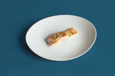 Maydanozlu limonlu somon filetosu, beyaz tabakta sarımsak ve dokulu mavi stüdyo arka planı. Balık ve sağlıklı yiyecek.