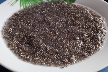 Soaked chia seeds on a white dish decorated with painted green leaf motifs. Superfood and health.