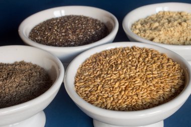 Close-up of a small plate filled with flax seeds surrounded by bowls of whole and powdered flax and chia seeds. Food and healthy diet.