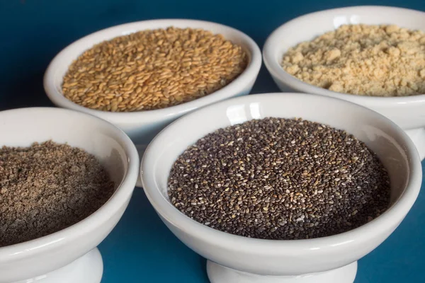 Close-up of a bowl with chia seeds along with small dishes with whole and powdered chia and flax seeds. Food and healthy diet.