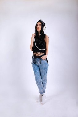 Kulaklıklı, gri arka planda müzik dinleyen güzel bir genç kadının tam boy portresi.