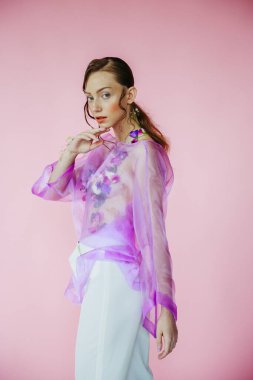 Stüdyonun arka planında pembe ceketli, parlak makyajlı pembe bluzlu bir kızın portresi.