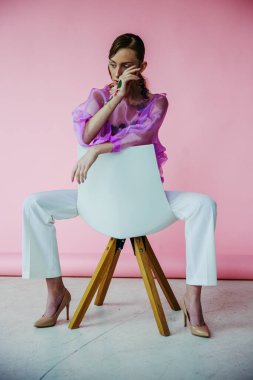 Pembe ve mavi elbiseli güzel bir kızın portresi beyaz bir sandalyede.