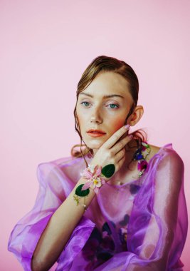 Güzel bir kız, şeffaf mor bir bluz ve zarif bir saç modeli olan taze çiçeklerle sütyen giyiyor.