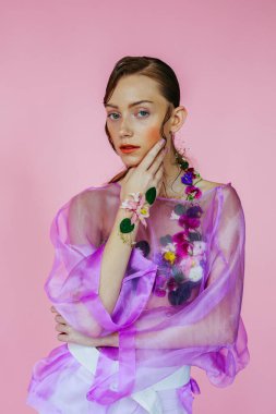 Güzel bir kız, şeffaf mor bir bluz ve zarif bir saç modeli olan taze çiçeklerle sütyen giyiyor.