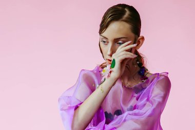 Güzel bir kız, şeffaf mor bir bluz ve zarif bir saç modeli olan taze çiçeklerle sütyen giyiyor.