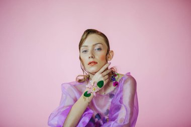 Güzel bir kız, şeffaf mor bir bluz ve zarif bir saç modeli olan taze çiçeklerle sütyen giyiyor.