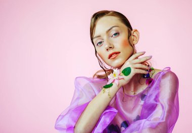 Güzel bir kız, şeffaf mor bir bluz ve zarif bir saç modeli olan taze çiçeklerle sütyen giyiyor.