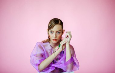 Güzel bir kız, şeffaf mor bir bluz ve zarif bir saç modeli olan taze çiçeklerle sütyen giyiyor.