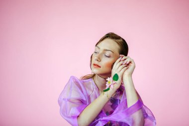 Güzel bir kız, şeffaf mor bir bluz ve zarif bir saç modeli olan taze çiçeklerle sütyen giyiyor.