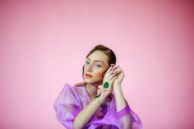 Güzel bir kız, şeffaf mor bir bluz ve zarif bir saç modeli olan taze çiçeklerle sütyen giyiyor.