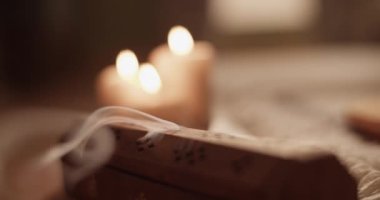 Evdeki meditasyon sırasında yanan mumların yanında aromatik duman yayan kereste tütsü kutusunun el kamerası görüntüsü.
