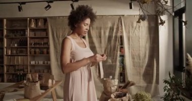 Çevrimiçi müşterilerin siparişlerini paketlerken organik ürünlerle birlikte Afro saçlı kağıt torbalı etnik bir kadın.
