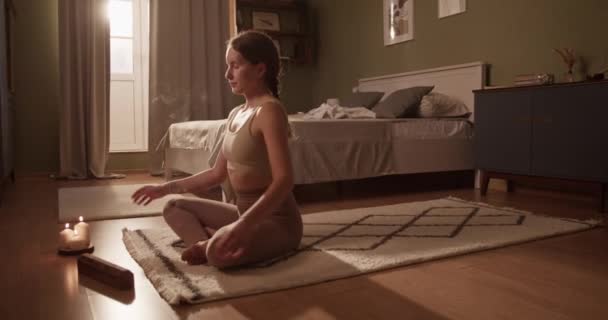在卧室瑜伽课上 身着运动服的年轻女性交叉腿坐在靠近芳香蜡烛的垫子上 做着坐姿 手持式拍摄 — 图库视频影像