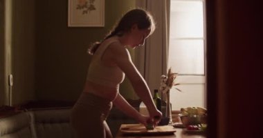 Evde güneşli mutfakta sağlıklı yemek hazırlıkları sırasında ketojenik salata için taze avokado kesen genç bir kadının el kamerası görüntüsü.