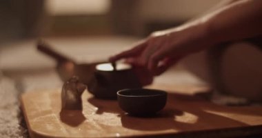 Anonim bir kadın paspasın üzerinde oturur ve evde yoga sırasında aromatik mumlar ve tütsü eşliğinde geleneksel Çin çayını bardağa doldurur.