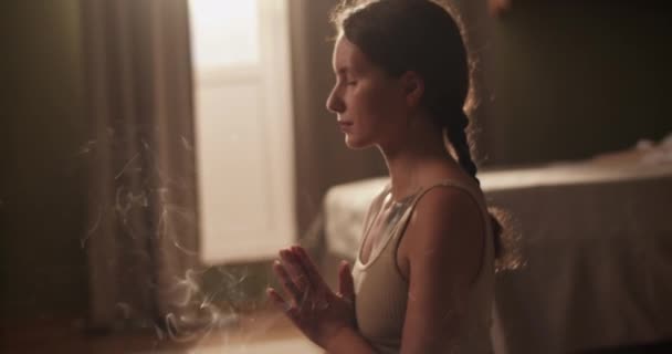 朝早く家でヨガセッション中にお香の煙と瞑想を呼吸祈りの手と閉じた目を持つ穏やかな女性の手のショット — ストック動画