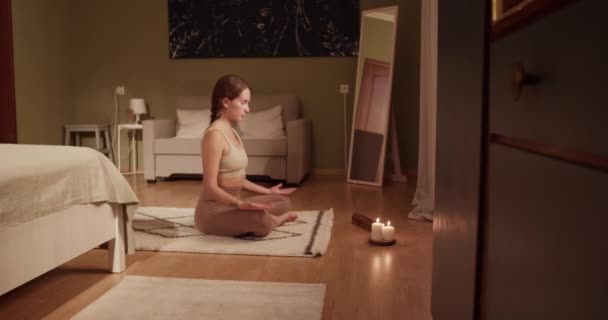 在家里的瑜伽课上 一只赤脚的年轻女子手牵手 坐在莲花上沉思 手牵手在床边的垫子上 还有芬芳的蜡烛 — 图库视频影像