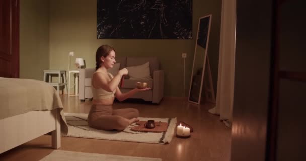 早晨在家里的卧室里 身着运动服的年轻女性在冥想课上 双腿交叉地坐在托盘边喝茶 弹奏着小夜曲 — 图库视频影像