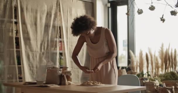 携帯電話でアフリカの髪を持つ若い民族の女性は 自分の環境に優しい店のためのウェブサイト上で作業しながら テーブルの上にエコ製品の写真を撮る — ストック動画