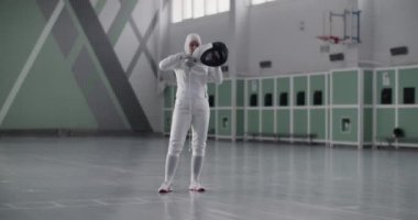Spor salonunda eskrim yaparken formalı, koruyucu maske takan ve kollarını kavuşturan tam vücut Müslüman sporcu kadın.