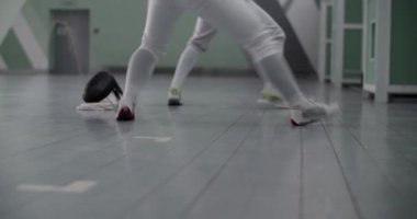 Beyaz üniformalı ve spor ayakkabılı, spor salonundaki eskrim antrenmanı sırasında aynı anda maskenin yanında hareket eden anonim sporcu kadınların zemin seviyesindeki statik görüntüleri.
