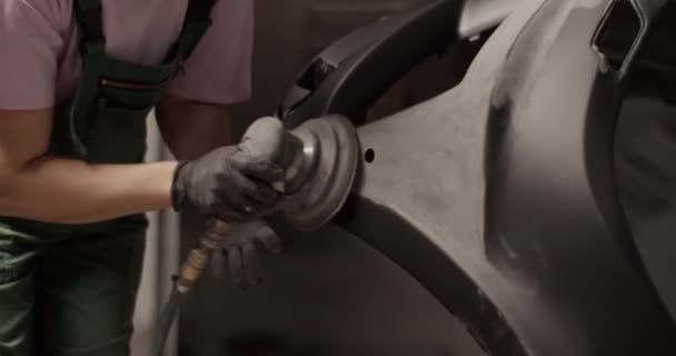 プロのガレージで詳細をペイントする準備をしながら 作業服の黒い車のバンパーに生姜の女性の手の込んだショットを傾ける — ストック動画