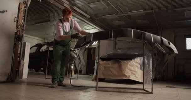 ガレージでの作業中に塗装車のバンパーをバッファリング均一で全身職人の女性のハンドヘルドショット — ストック動画