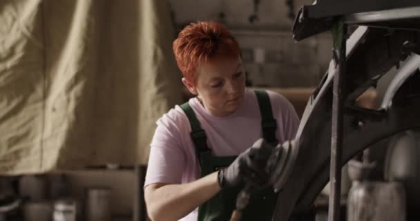 浅角手持式红头发女工匠在日光浴车间工作时穿着工作服坐在后排和砂车保险杠上的照片 — 图库视频影像