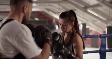 Spor salonunda boks antrenmanında erkek eğitmenin zırhını yumruklayan agresif kadın boksörün el kamerasıyla çekilmiş fotoğrafı.
