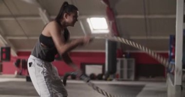 Spor salonundaki işlevsel eğitim sırasında at kuyruklu bir kadının savaş halatlarıyla egzersiz yaparken elde çekilmiş fotoğrafı.