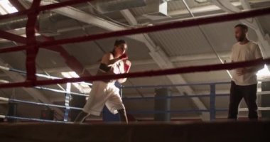 Spor salonundaki boks antrenmanı sırasında koçun tavsiyesini dinlerken el kamerasıyla havayı yumruklayan sporcu kadının düşük açılı görüntüsü.