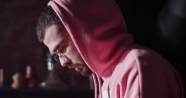 Tilt down man in hoodie standing at bar counter and putting tobacco in ceramic bowl of hookah