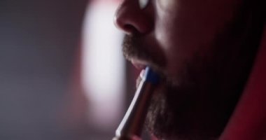 Side view cropped man with beard drawing on hookah and exhaling dense smoke while chilling in lounge bar