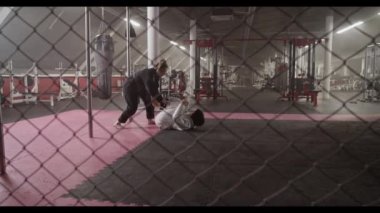 Handheld shot of Muslim woman in hijab and gi pushing away from female coach during Brazilian jiu jitsu training in gym