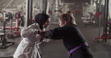 Zoom in view of Muslim female fighter throwing away hands of opponent while sparring during BJJ training in gym