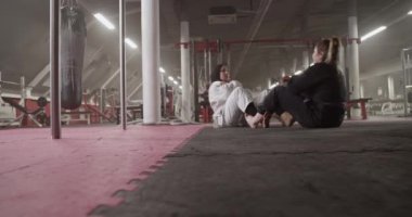 Handheld shot of multiracial women giving high fives and doing sit ups on floor during grappling training in gym