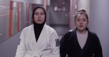 Tracking shot of female coach touching shoulder and speaking with Muslim wrestler while walking in corridor of gym before BJJ training